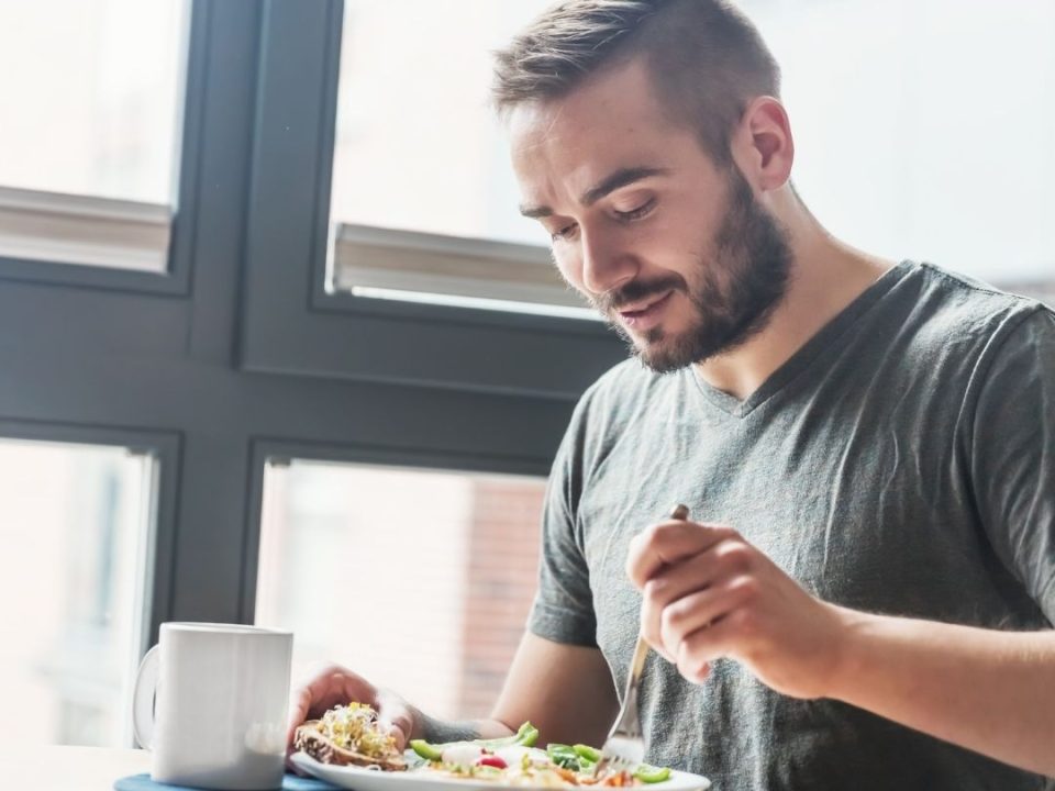 Man with a beard eating a healthy meal by a window